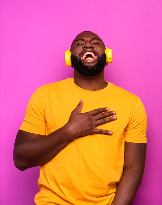 Happy man wearing yellow T-shirt and yellow headphones in front of a brightly colored pink background