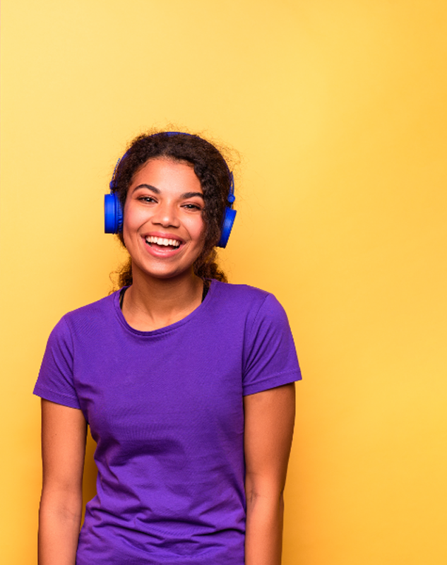 Lady smiling wearing bright blue headphones, standing in front of a bold yellow background